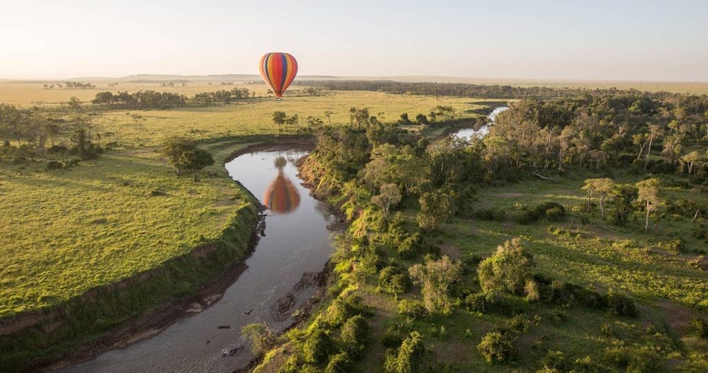 Hot air balloon safari over Maasai Mara at sunrise with river and wildlife below