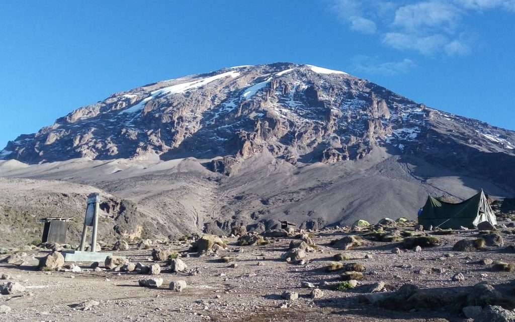 Wooden A-frame Horombo Huts on the Marangu Route with Mount Kilimanjaro's Kibo peak in the background during sunset
